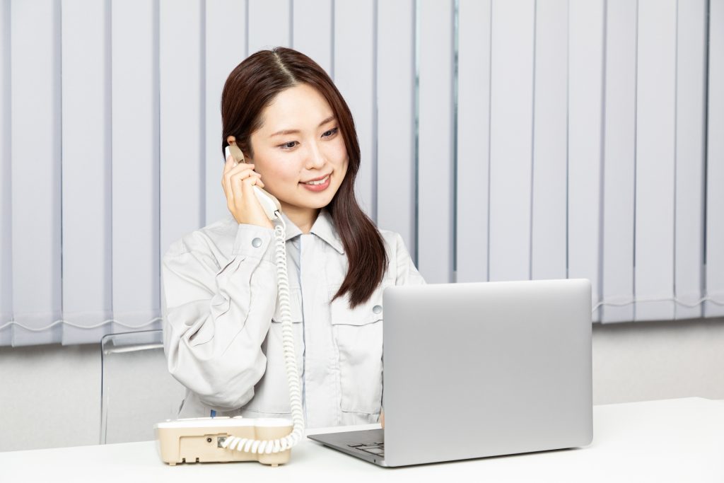 火災保険申請の相談に対応する調査スタッフ（作業服の女性）がパソコンを見ながら電話応答している写真