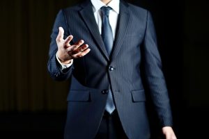 暗い背景でスーツを着た人物が手のひらを上に向けている写真