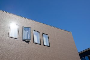 青空の下に立つ住宅。窓ガラスに反射する太陽光が、遮熱や断熱など塗料の性能を象徴している。